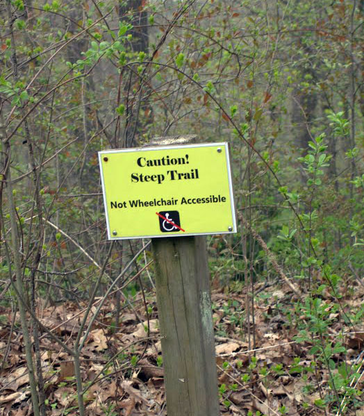 Sign in the woods that reads Caution! Steep Trail, Not Wheelchair Accessible.