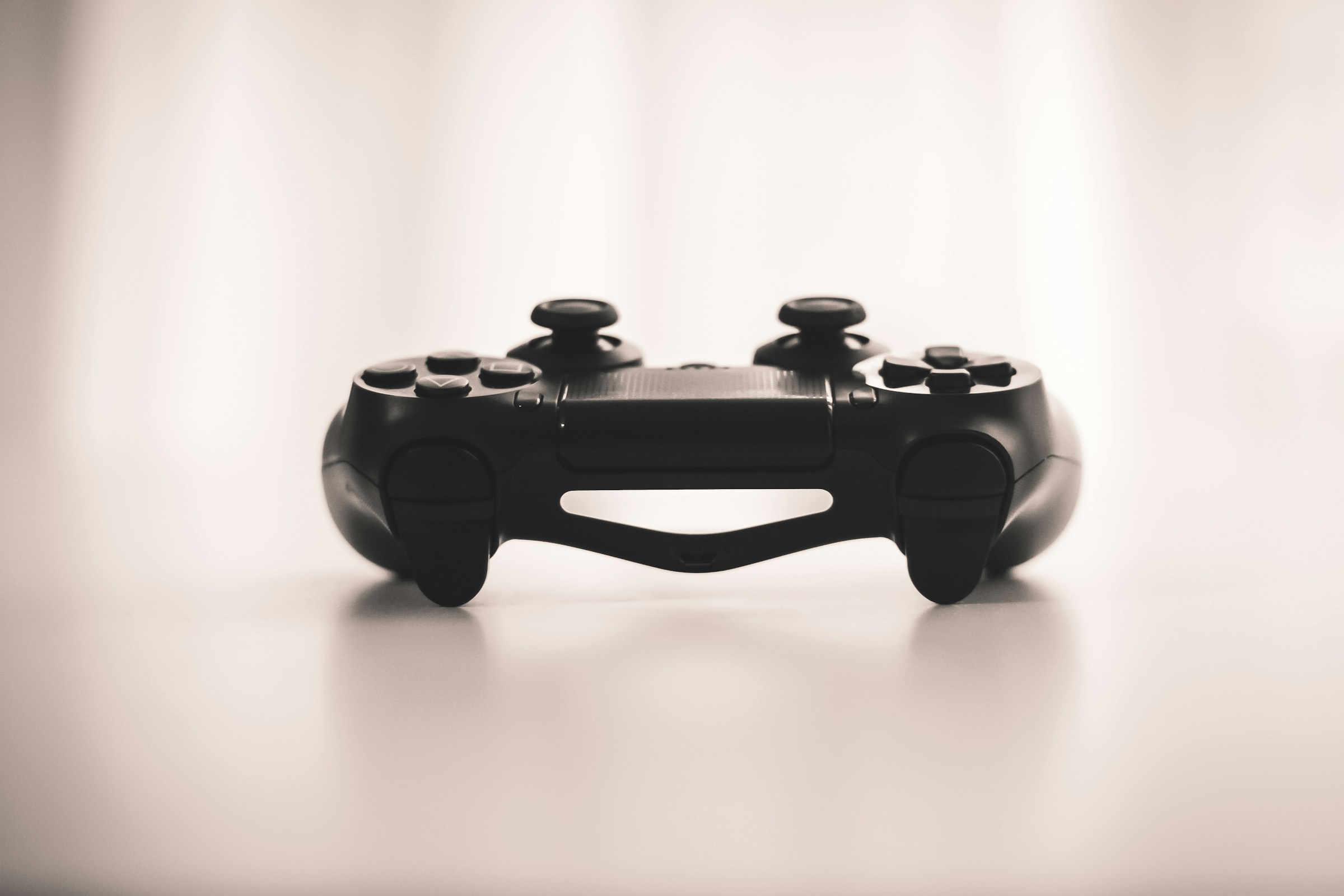 Image is primarily decorative. Depicts a Playstation Controller resting on a table in which the indicator light on the top of the controller is most visible. This article is about video games.