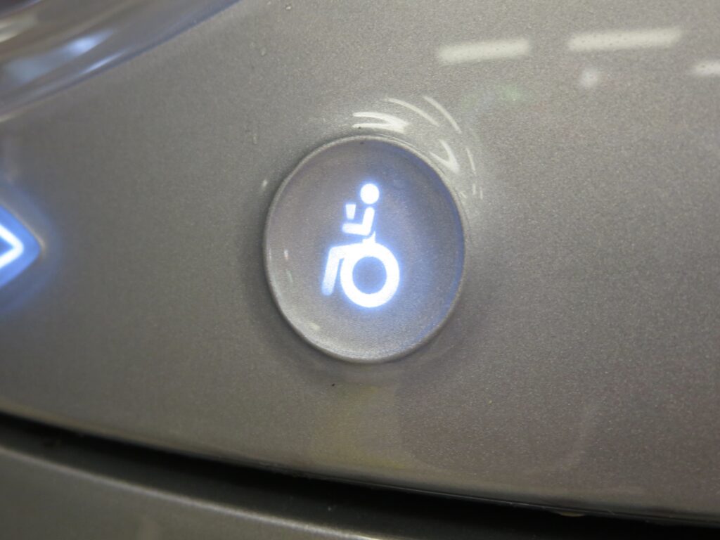 Accessibility button on a Coke machine. The button features an icon of a wheelchair user holding a cup.