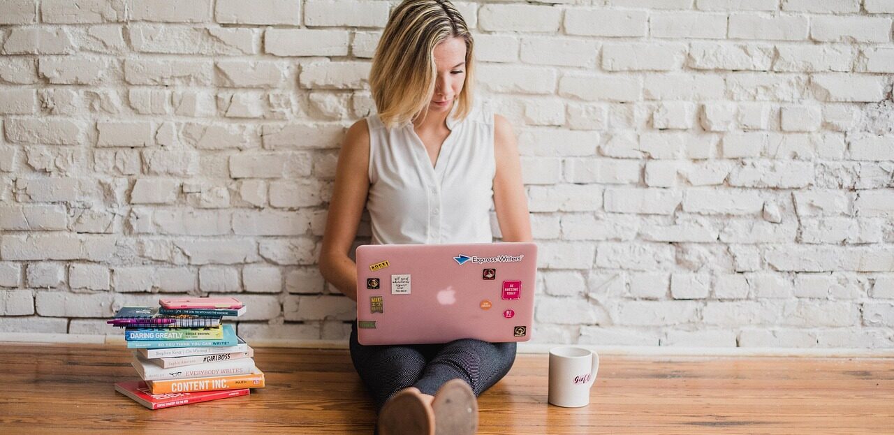 Student works on her laptop, a stack of books on one side and a coffee mug on the other.